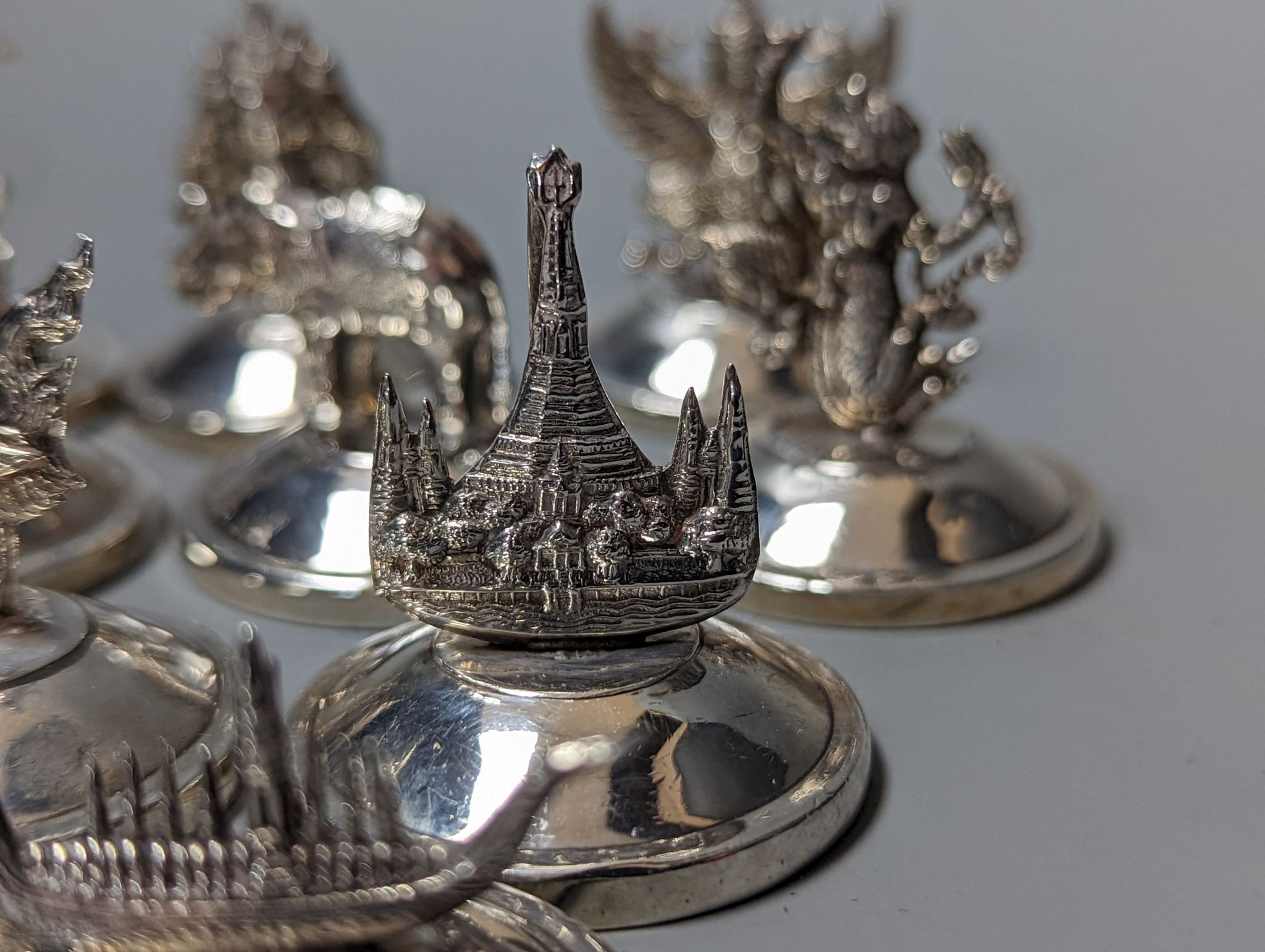 Sixteen assorted Siamese sterling mounted menu holders, modelled with figures, elephant, etc.